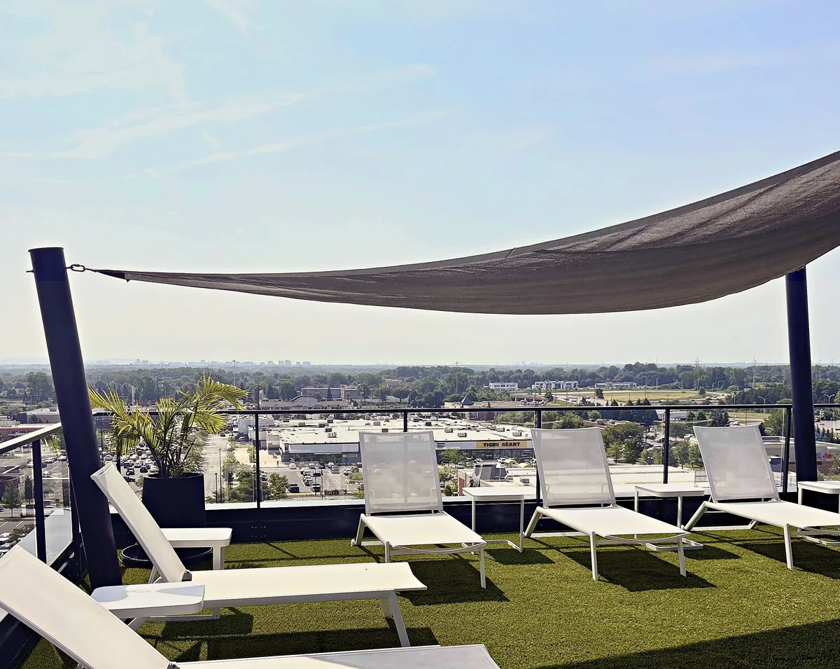 Terrasse sur le toit : chaises longues blanches sous une voile d'ombrage, avec vue sur Boisbriand